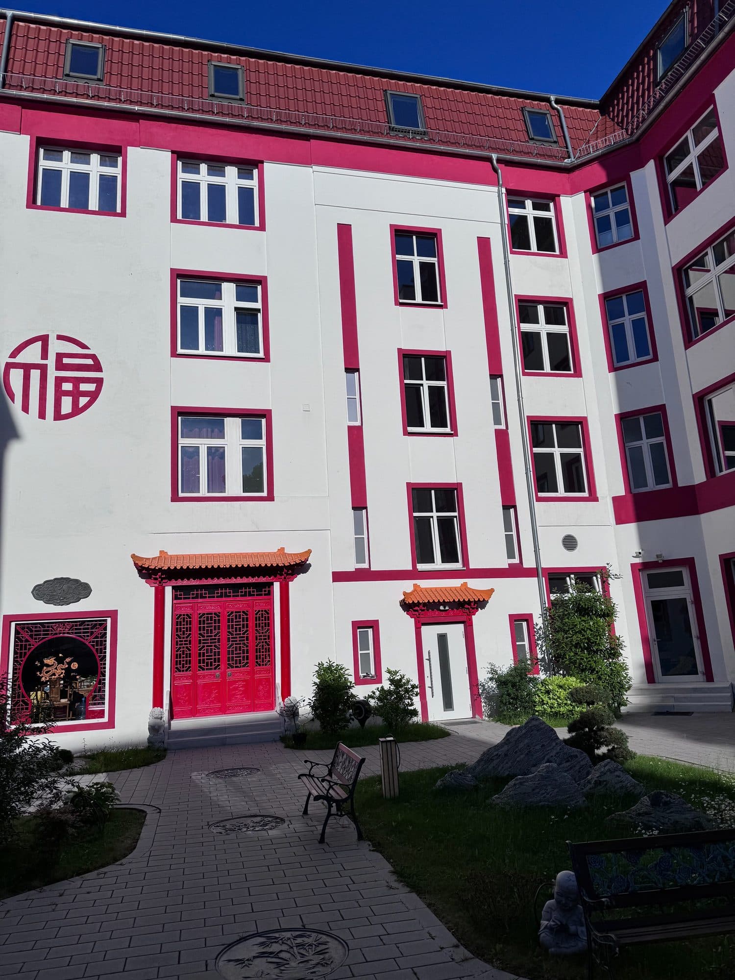 Sitzbänke und Steingarten vor der Fassade mit chinesischem Glücksmedaillon