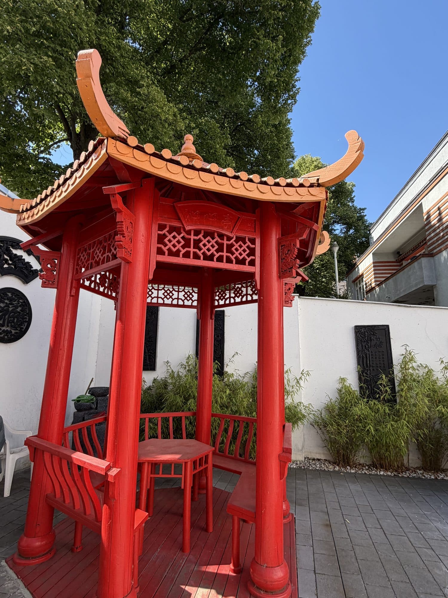Roter chinesischer Holzpavillon mit geschwungenem Dach und Sitzgelegenheiten