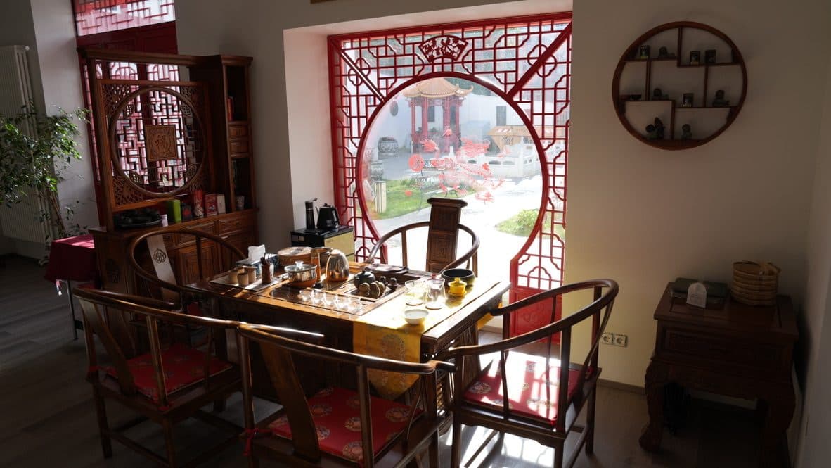 茶桌与座椅,背后是红色月洞窗,窗外是庭院凉亭
